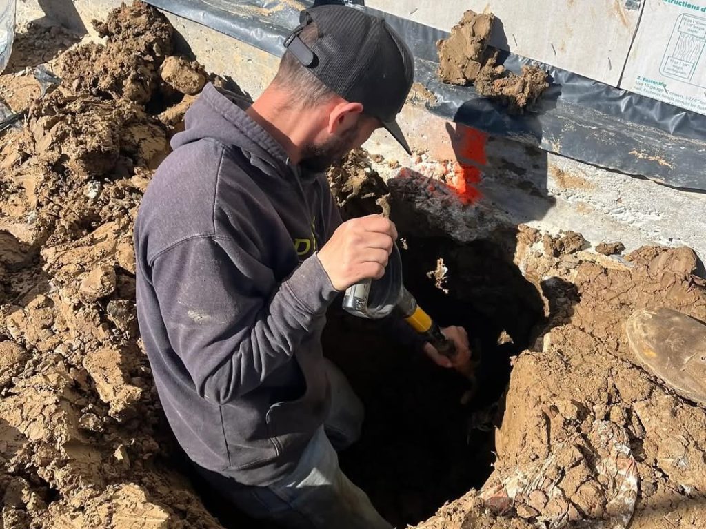 An FnD Piers team member is digging around a concrete foundation in order to figure out how to repair the foundation the best.