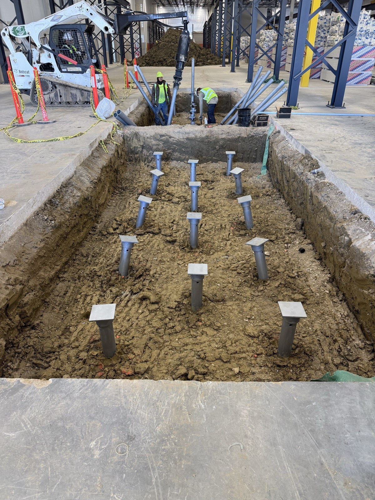 FnD Piers crew installing helical piers in an excavated foundation trench at an indoor commercial jobsite