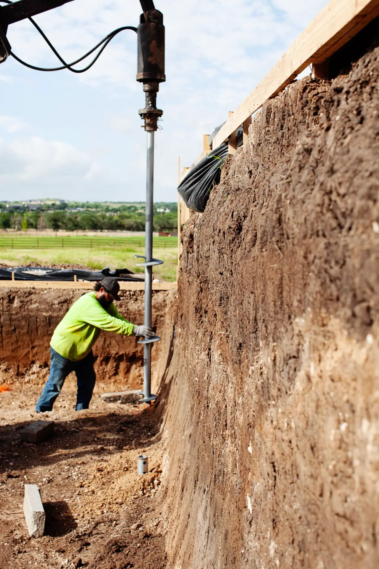 FnD Piers crew member guiding a helical pier auger into an excavated foundation pit at a Texas jobsite