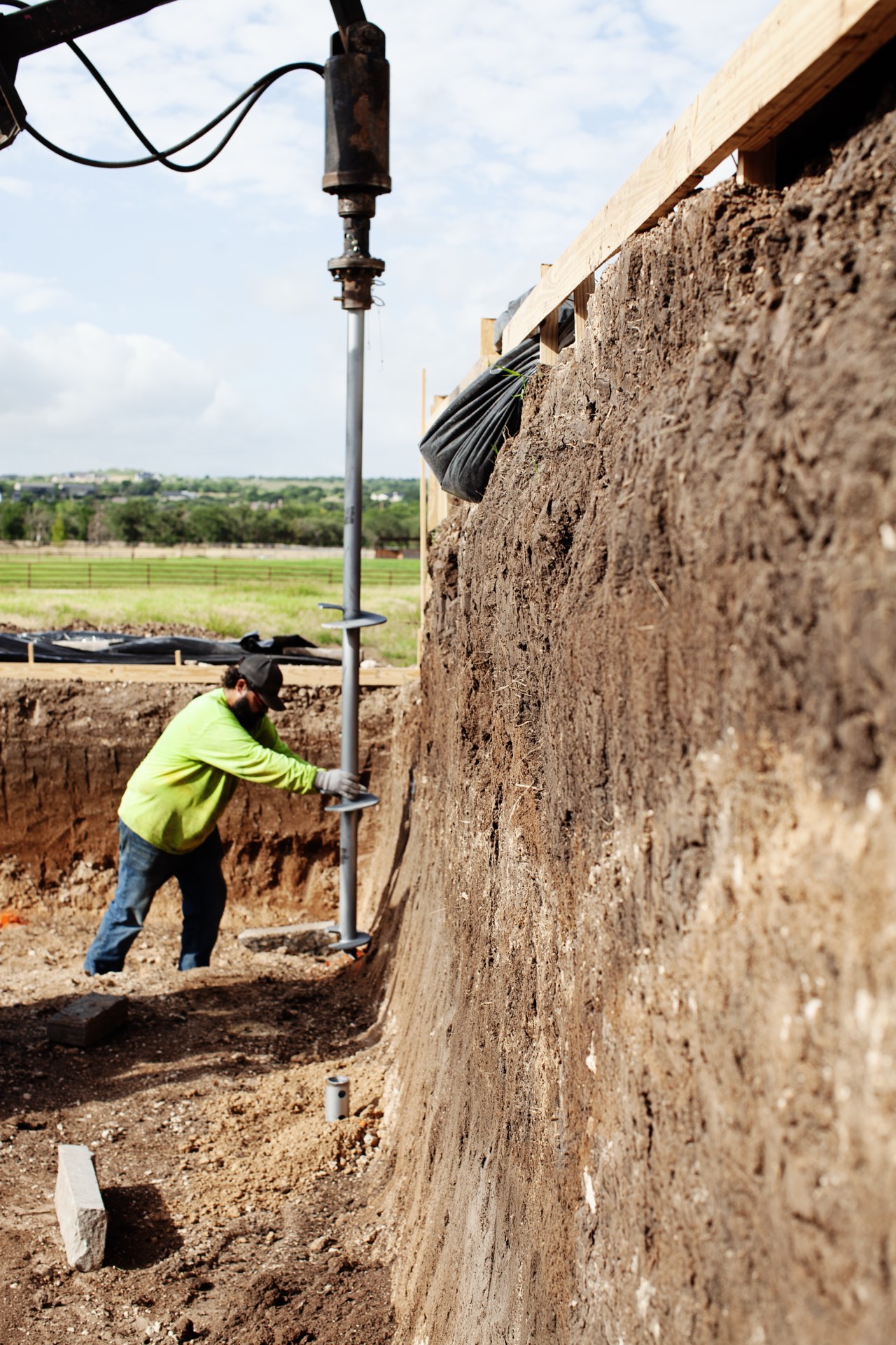 FnD Piers crew member guiding a helical pier auger into an excavated foundation pit at a Texas jobsite