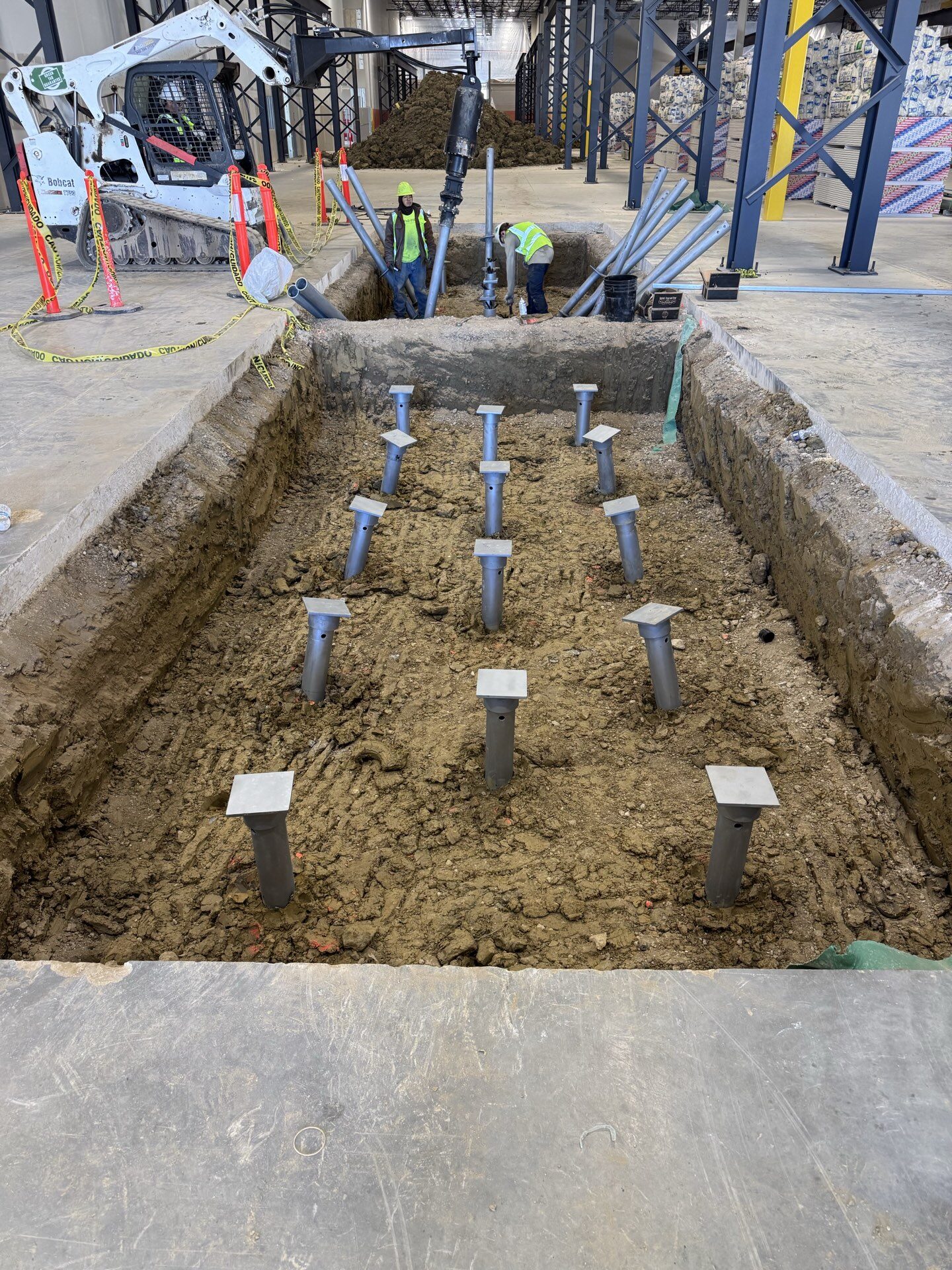 Grid of FnD Piers helical piers installed in an excavated pit inside a commercial building, with crew and rig