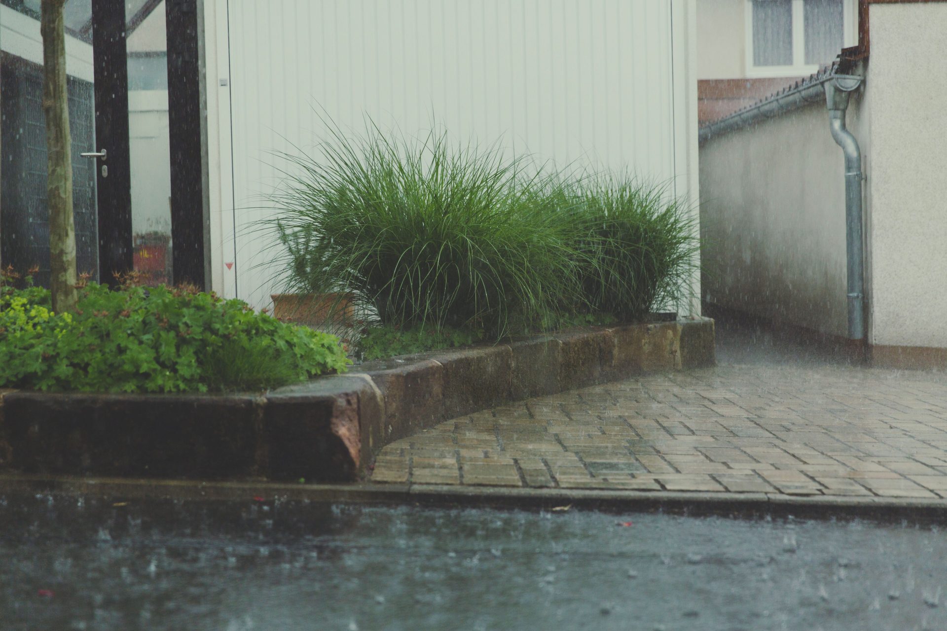 Rain draining from a downspout beside a home — seasonal foundation moisture management