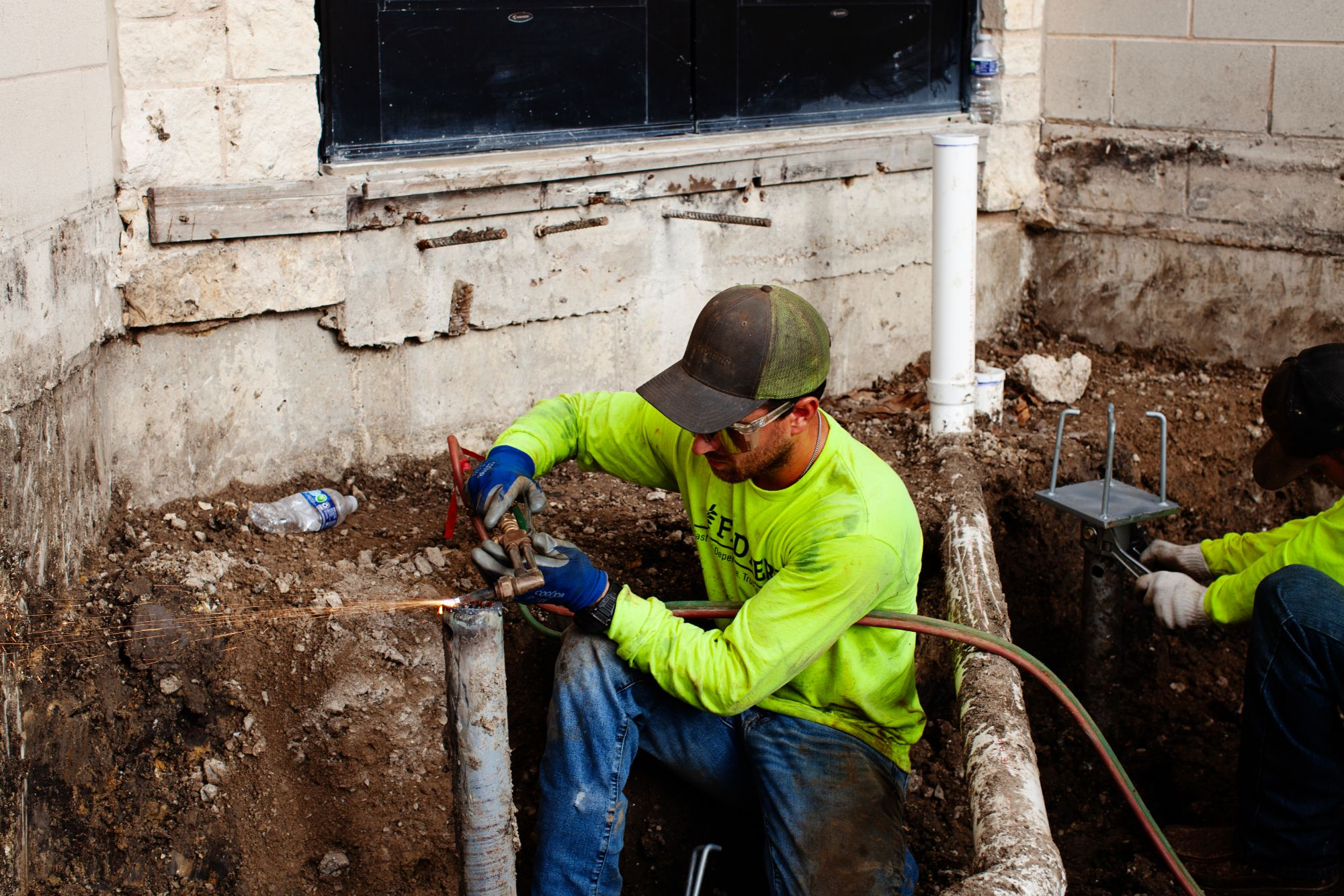 FnD Piers crew fitting a helical pier bracket during foundation repair on an existing building, serving Garland, TX