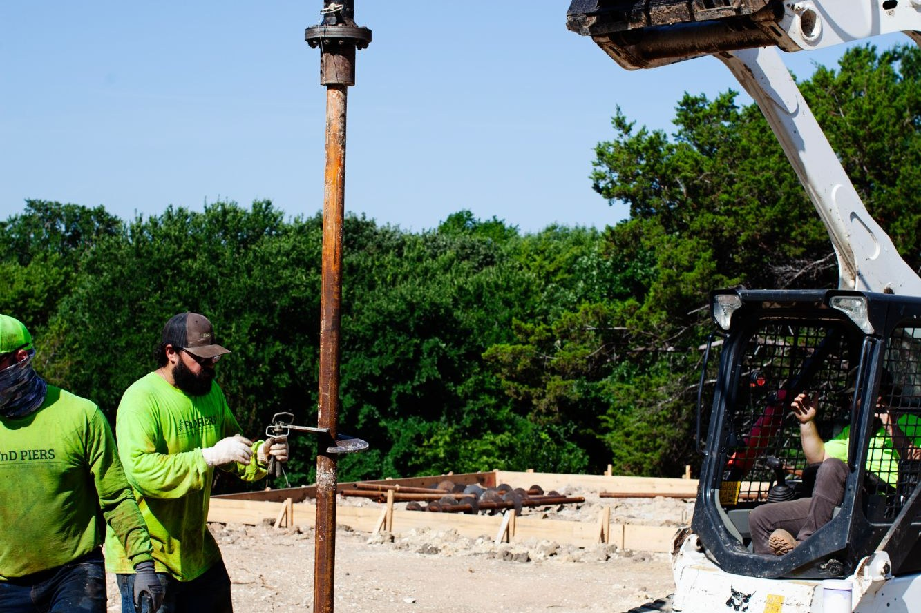 FnD Piers crew seating a helical pier under the drive head at a new construction site, serving Haslet, TX