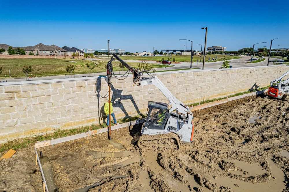 excavator installing helical piers in dirt
