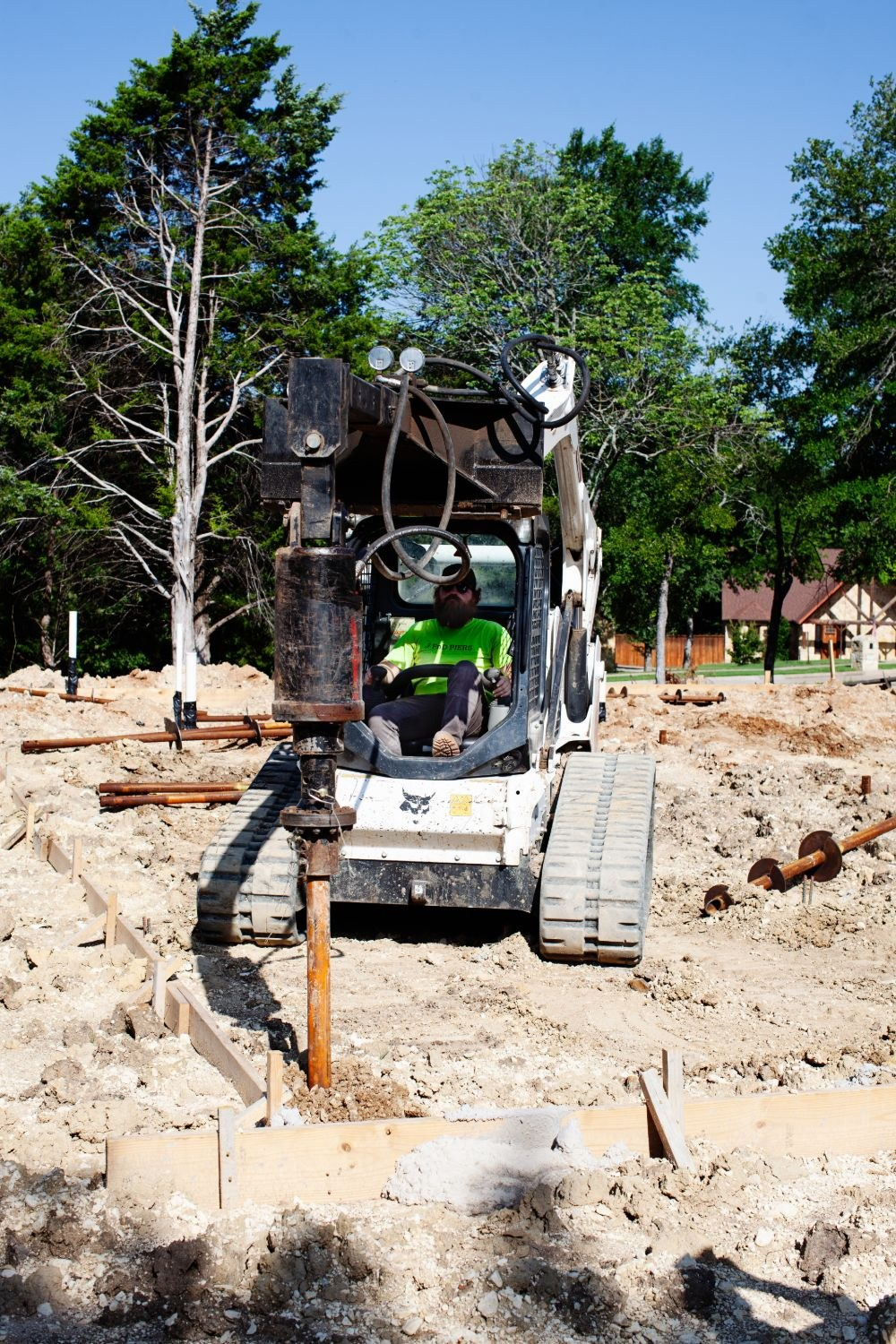 FnD Piers operator driving a helical pier with a skid steer beside footing forms, serving Haslet, TX