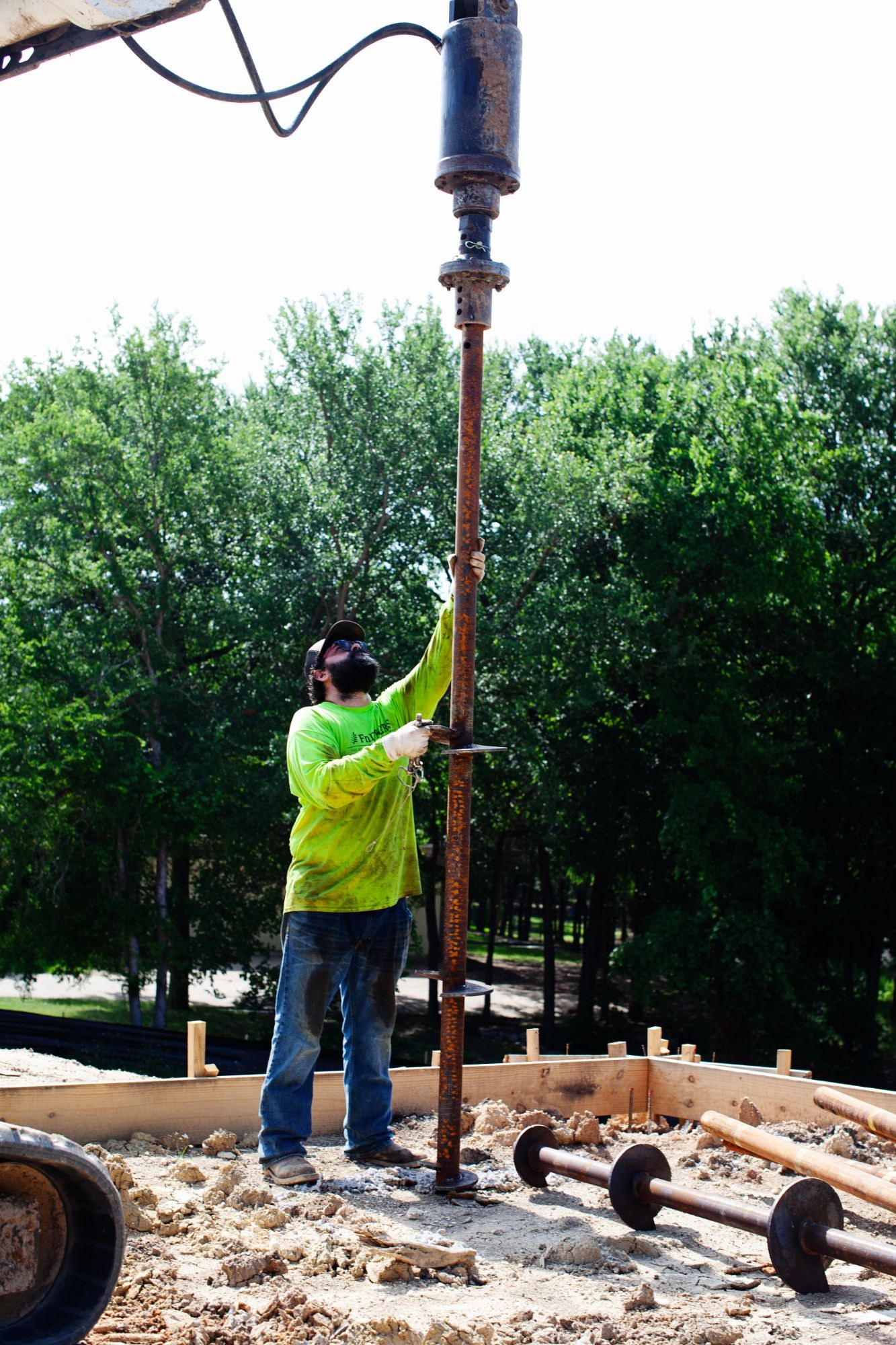 FnD Piers technician guiding a helical pier section under the drive head at a new construction site, serving Eagle Mountain, TX