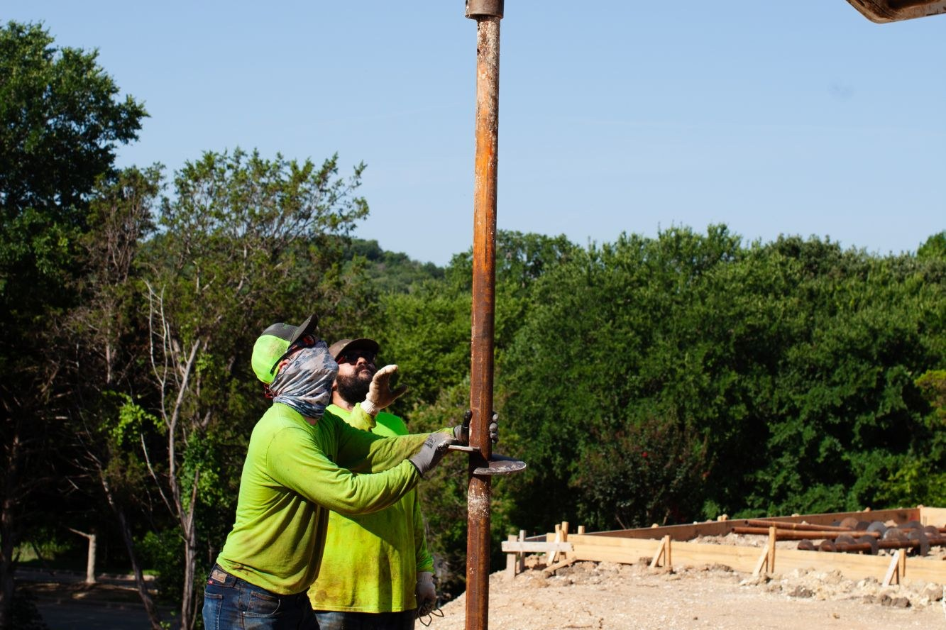 FnD Piers two-man crew seating a helical pier section under the drive head, serving Eagle Mountain, TX